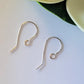 Gold earring hooks on a white surface with a green and white background