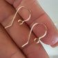 Gold earring hooks held between fingers against a neutral background