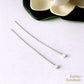 Two silver headpins on a white surface with a blurred flower in the background.