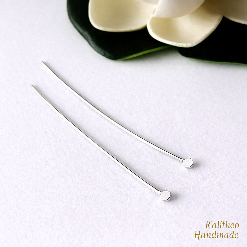 Two silver headpins on a white surface with a blurred flower in the background.