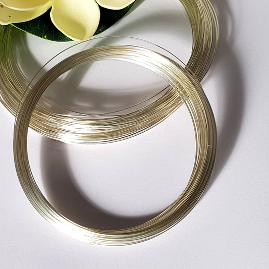 Two coiled pieces of 1.0mm round Argentium Silver 940 wire, placed on a white surface with a flower in the background.