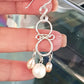Close-up of handmade chandelier pearl earring held in hand, showing intricate sterling silver wirework with white and soft-pink freshwater pearls – FKJ-210E by Kalitheo