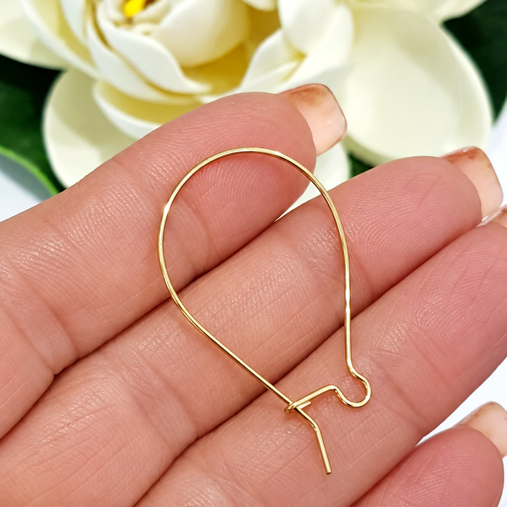 Single gold filled handmade kidney ear hook held in hand beside white magnolia flower, showing teardrop shape and locking closure detail