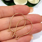 Pair of gold filled handmade kidney ear hooks held in hand beside magnolia flower, showing size and warm gold tone