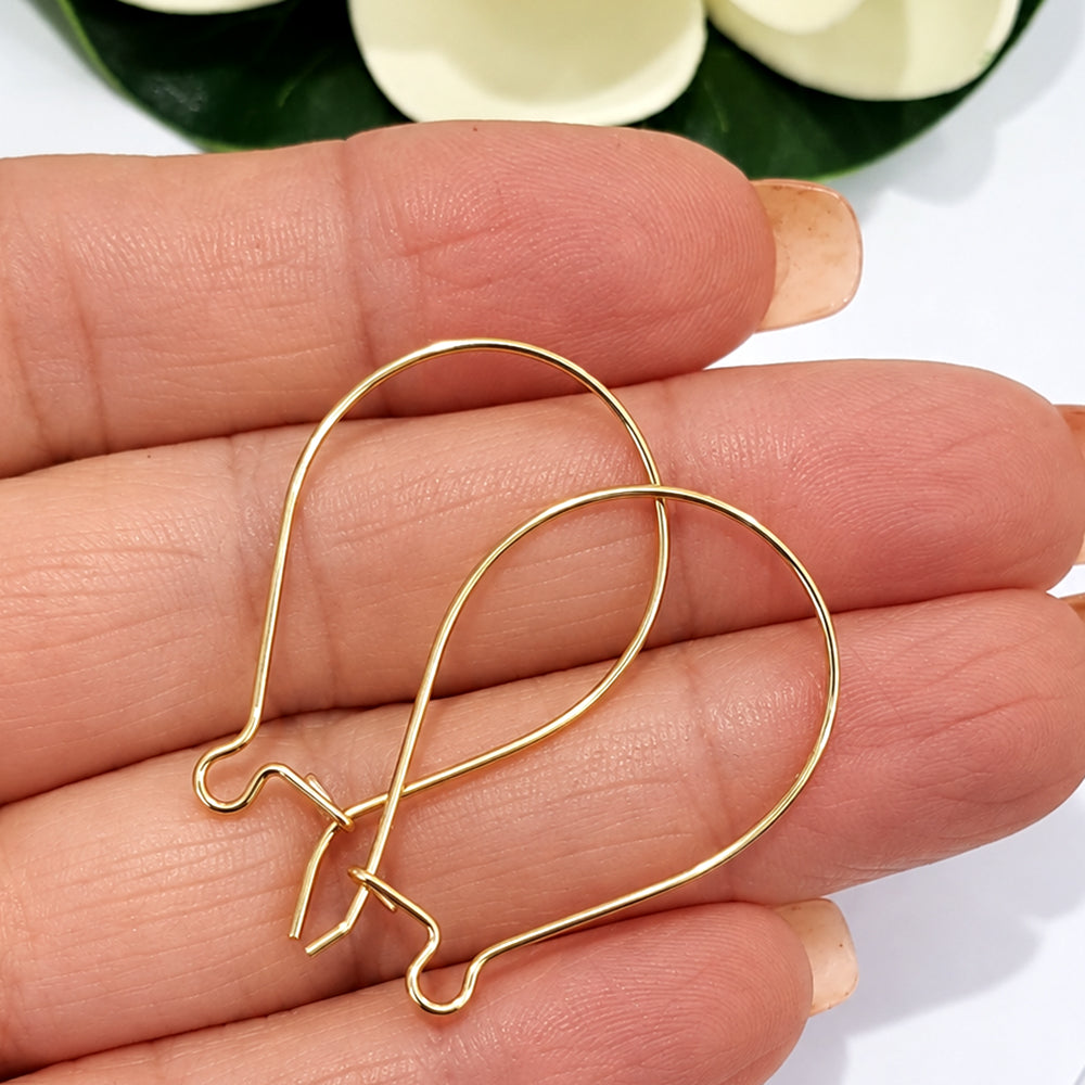 Pair of gold filled handmade kidney ear hooks held in hand beside magnolia flower, showing size and warm gold tone