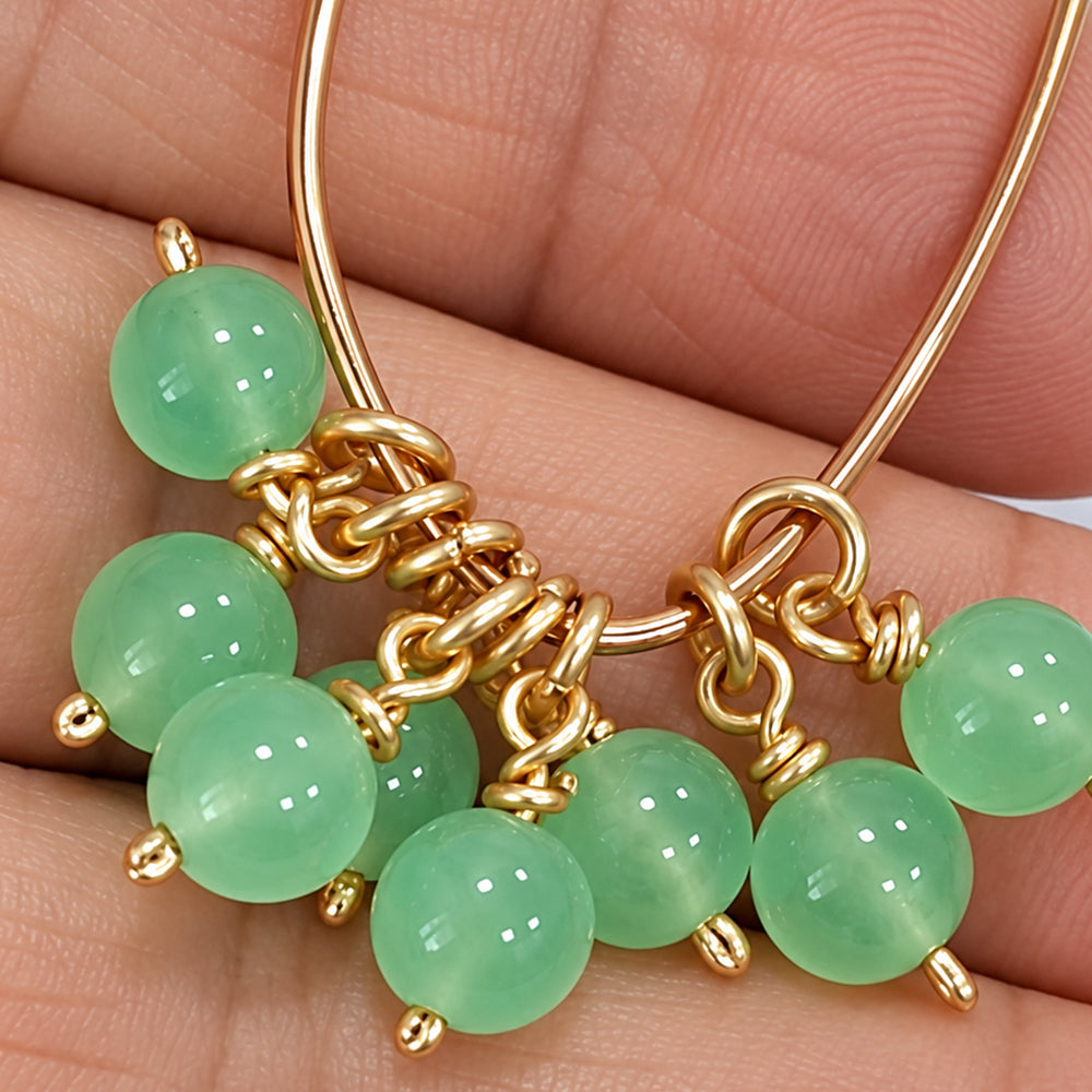 Close-up of handmade round jade bead dangles hanging from open jump rings on gold-coloured wire