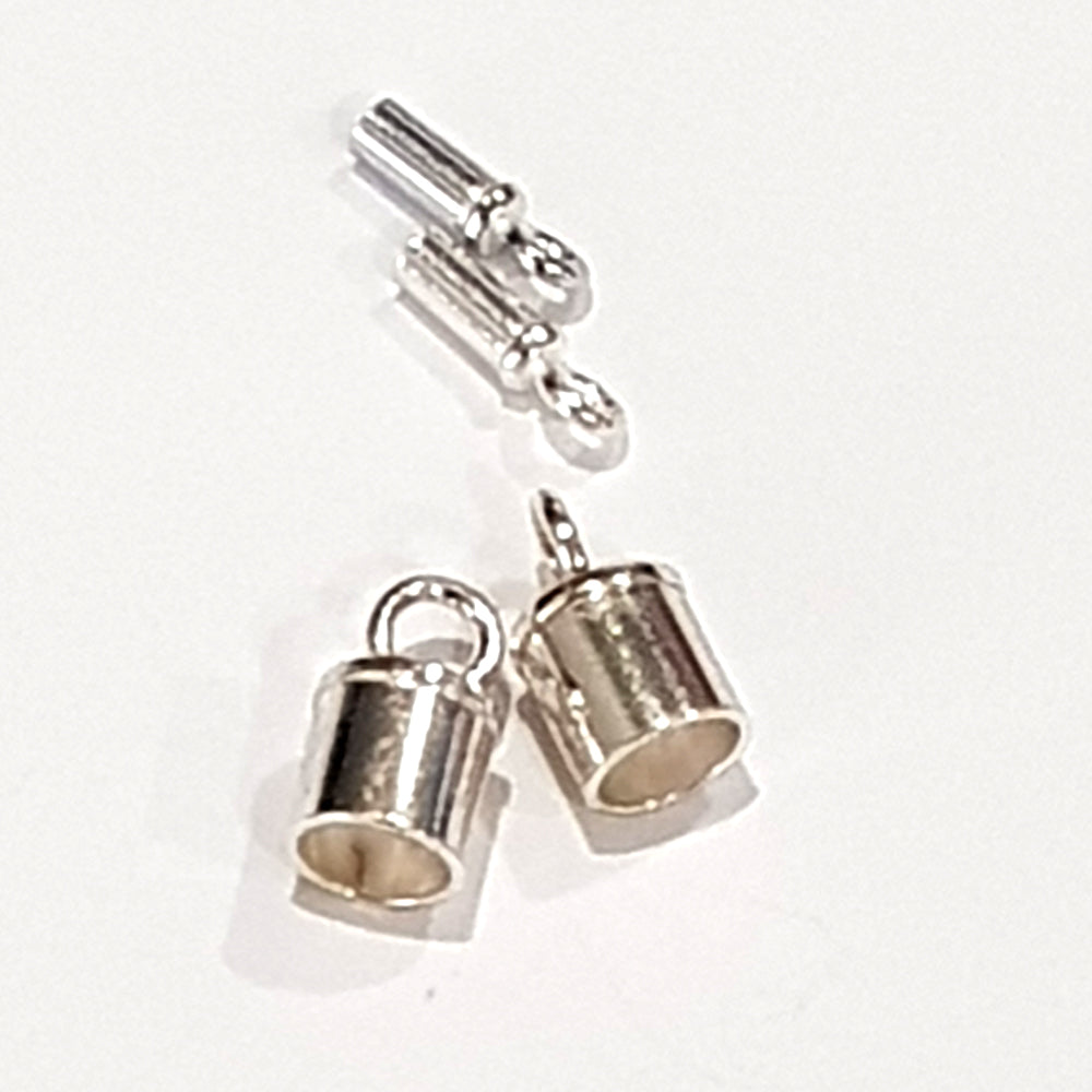 Close-up of two tiny sterling silver narrow tube end caps held on a finger, showing fine detail and small loop bail