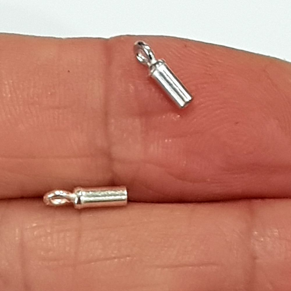 Two large sterling silver barrel tube end caps held in an open hand, showing the cylindrical form, open hollow interior, and loop bail