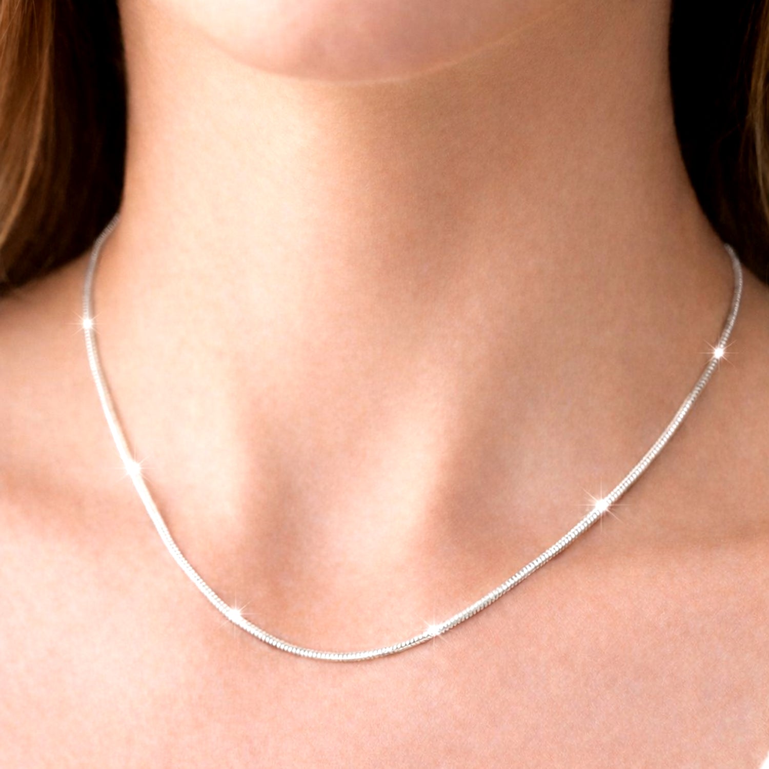 Silver necklace on a person's neck with a neutral background