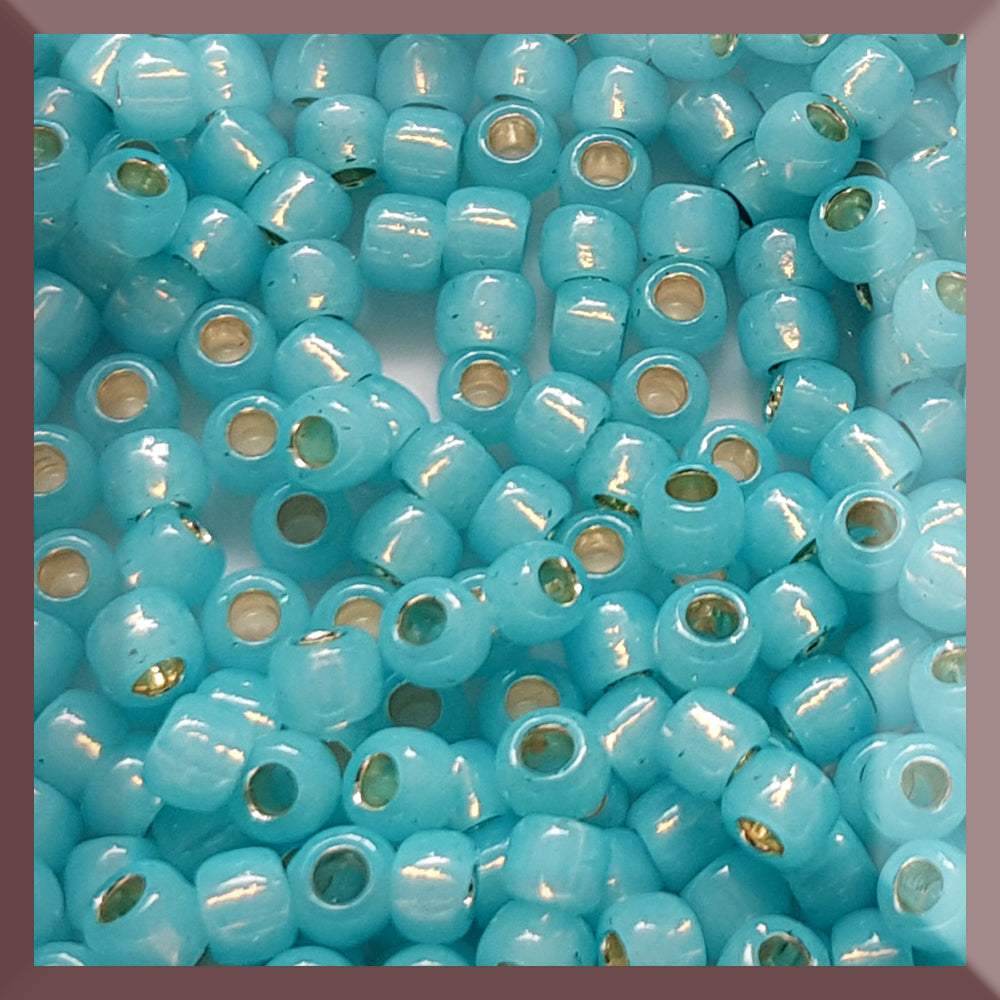 A close-up of round Toho seed beads in milky aqua color with silver lining, bead size 6/0.
