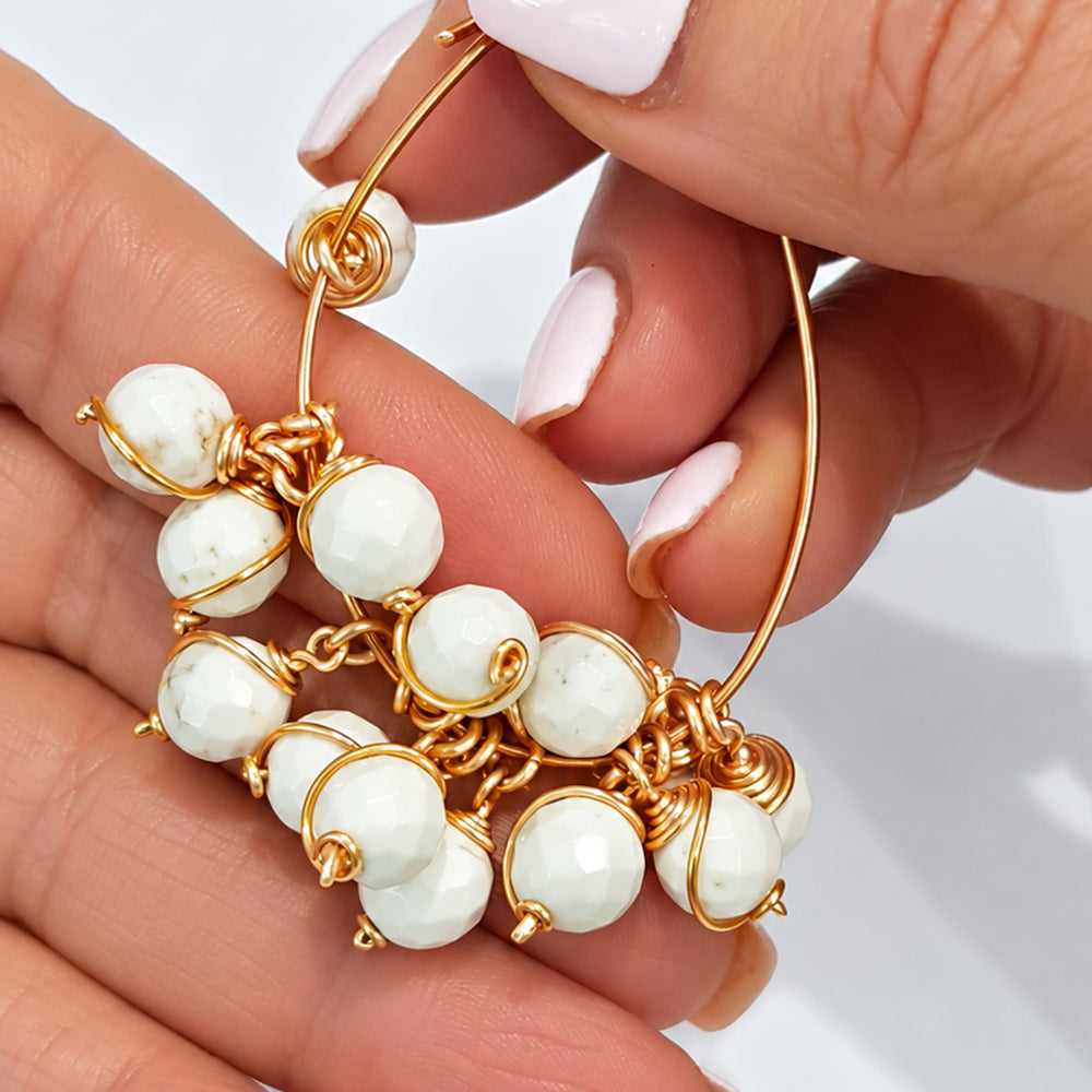 Close-up cluster of round white howlite bead drop dangles with natural grey veining and gold-coloured wire wraps