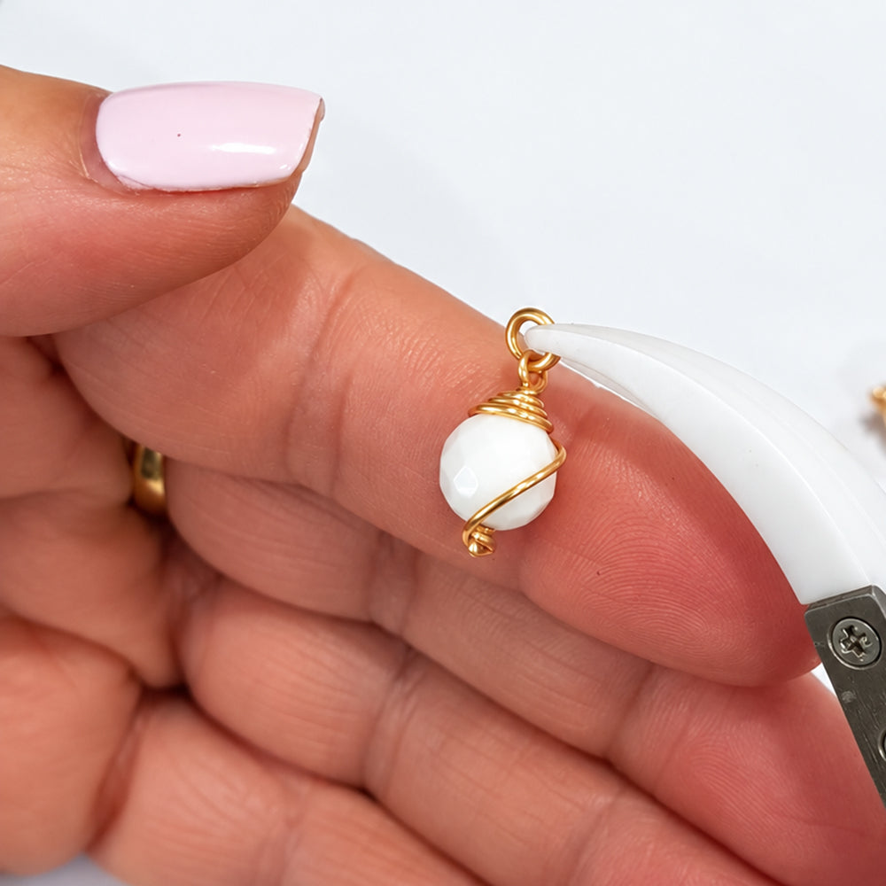 Close-up of an 8 mm white howlite bead drop dangle with spiral gold-coloured wire wrap and open jump ring held in pliers