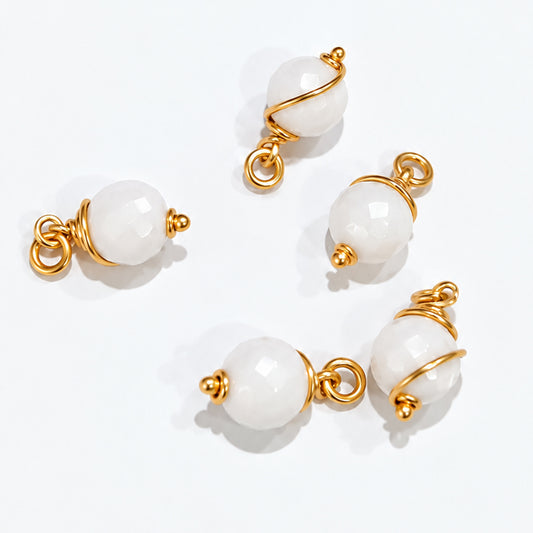 Cluster of handmade white howlite bead drop dangles hanging from a gold-coloured hoop and held in hand