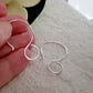 Large Hanging Loops For Resin Earrings between fingers showing the size with blurred flower background.