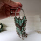 A hand holding a pair of beaded dangle earrings with green and brown beads on a silver wire hook. Repaired.