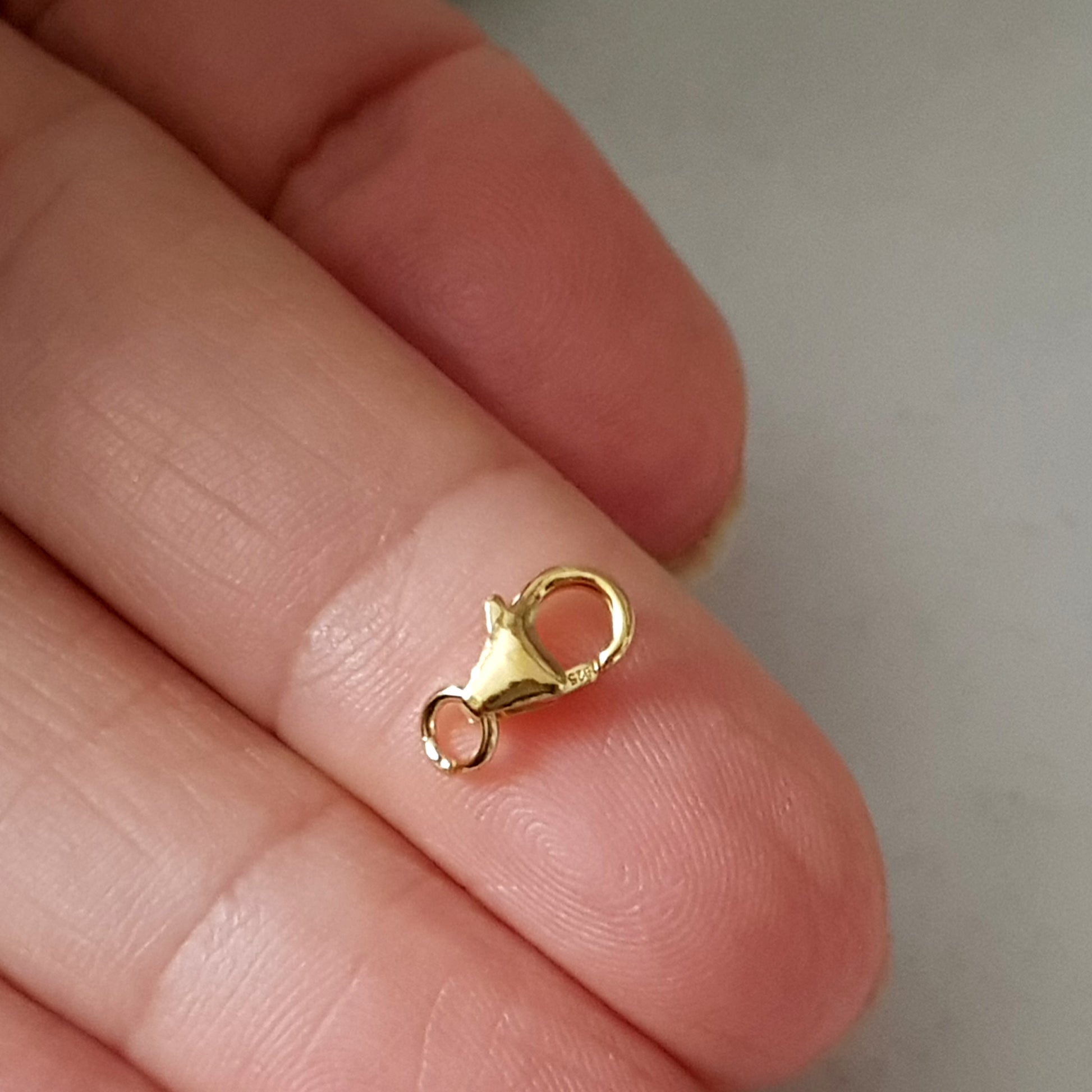 An 8mm gold-plated sterling silver lobster claw clasp held between fingers.