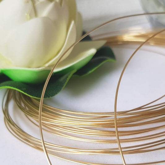 A spool of round 9ct yellow gold wire, with a green and white object partially visible in the background.