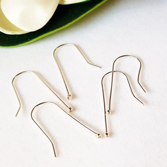 A set of sterling silver balled straight earring hooks laid out on a white surface, with a few hooks displaying a reflective shine.