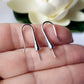 A pair of sterling silver earring hooks with pearl cups placed on a hand, with a flower in the background.