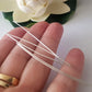 A hand holding a straight wire pin with a bundle of additional pins displayed in the background, alongside a white flower.