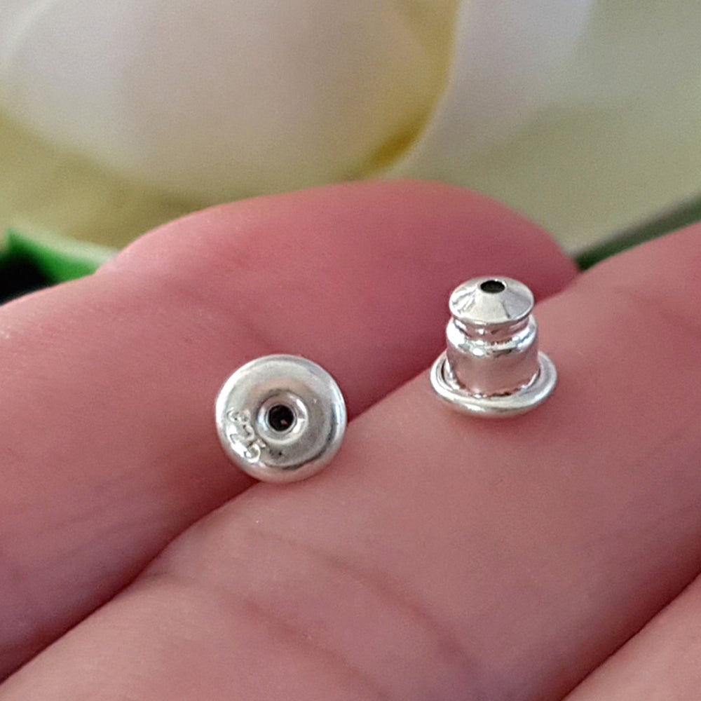A pair of sterling silver bullet style earring backs with memory rubber inserts placed on a person's hand.