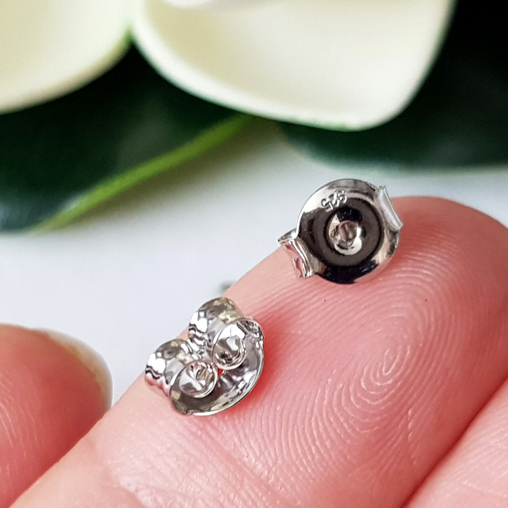 A pair of sterling silver 925 rhodium plated scroll earring butterfly backs on a person's fingertip.