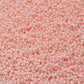 A round container filled with baby pink opaque luster Toho seed beads. close up.