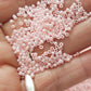 A round container filled with baby pink opaque lustre Toho seed beads. 11/0 on a hand