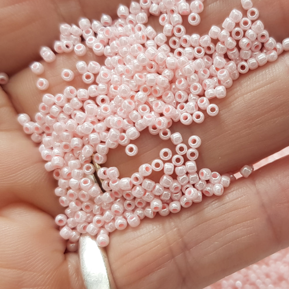 A round container filled with baby pink opaque lustre Toho seed beads. 11/0 on a hand