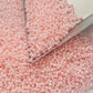 A round container filled with baby pink opaque luster Toho seed beads. 11/0 triangle scoop.