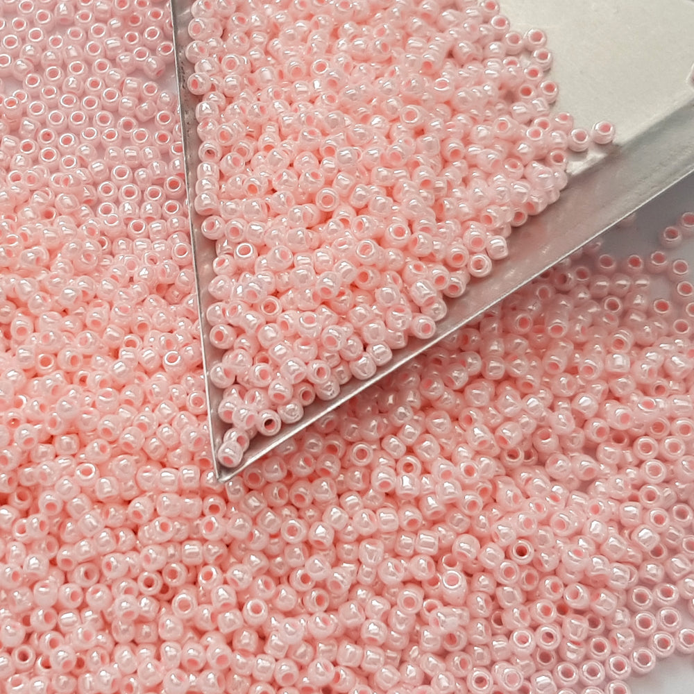 A round container filled with baby pink opaque luster Toho seed beads. 11/0 triangle scoop.