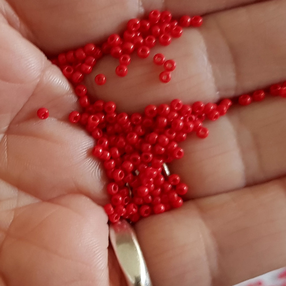 11/0 Toho seed beads in cherry red opaque on a hand.