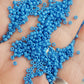 A close-up image of a bowl filled with round opaque cornflower blue Toho seed beads.