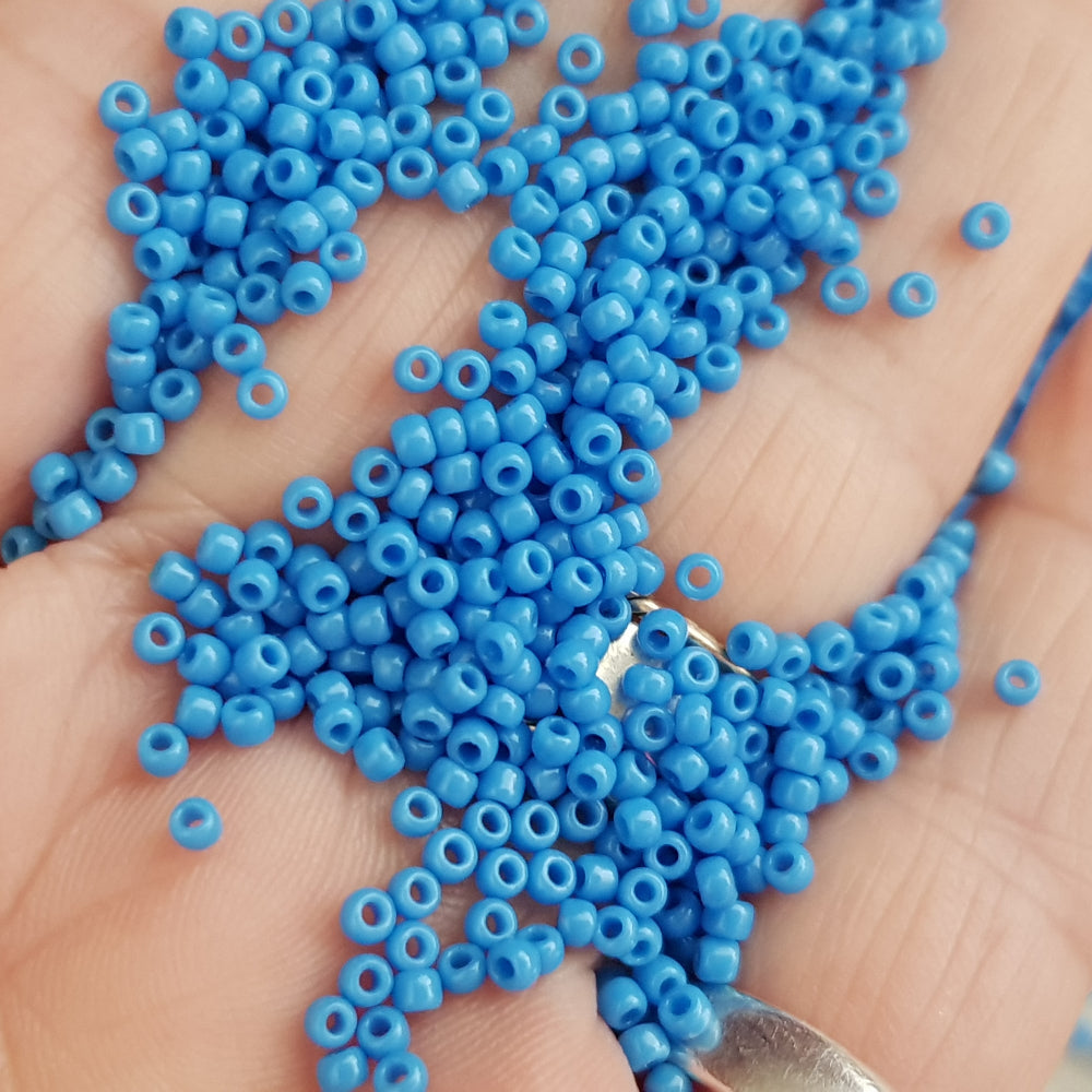 A close-up image of a bowl filled with round opaque cornflower blue Toho seed beads.