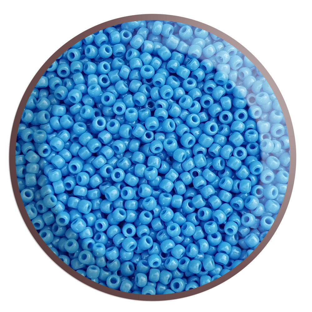 A close-up image of a bowl filled with round opaque cornflower blue Toho seed beads.