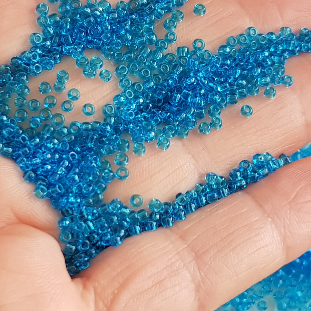 11/0 Toho seed beads in dark aquamarine transparent on a hand.