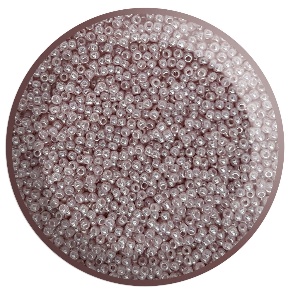 A pile of round Toho seed beads in Grape Mist Ceylon colour 11/0 in a circle with white background,