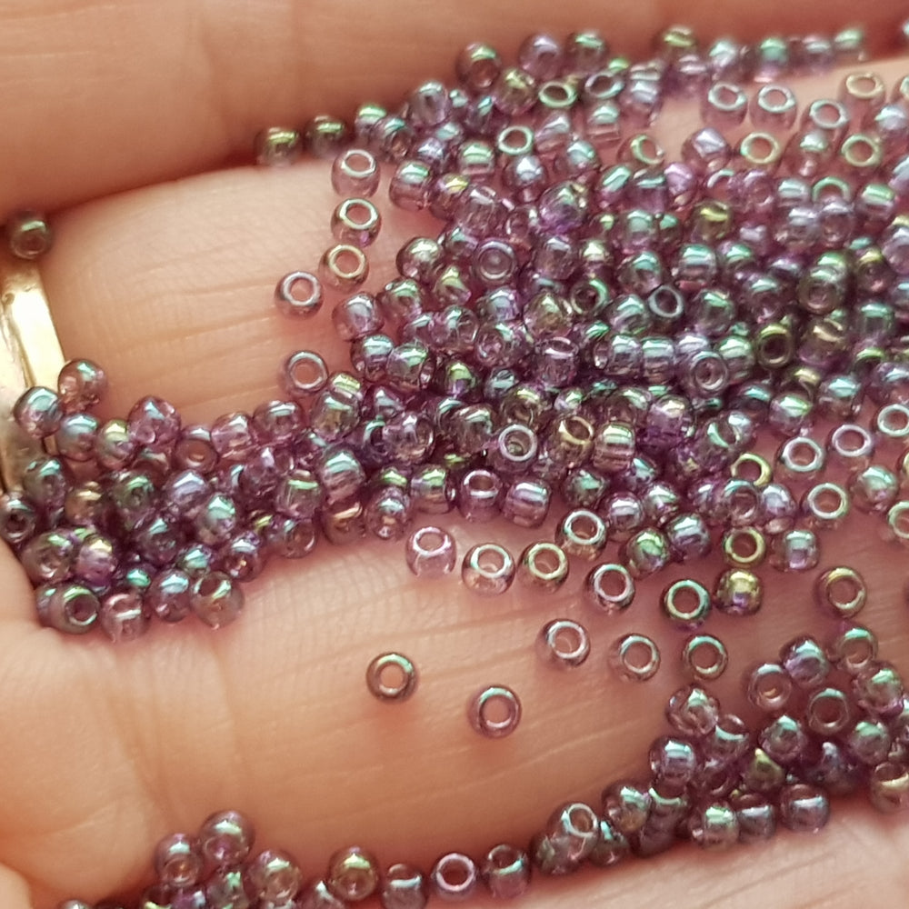 A close-up view of Hydrangea Gold Luster Round Toho Seed Beads 11/0 showing their lustrous finish and multicolored appearance. on a hand.