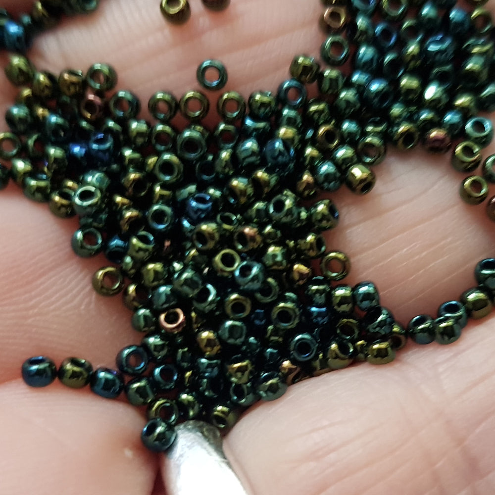 11/0 Toho Seed Beads in Iris green/brown metallic TR-84 on a hand close up.