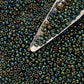 11/0 Toho Seed Beads in Iris Green/Brown Metallic TR-84 with a beading scoop.