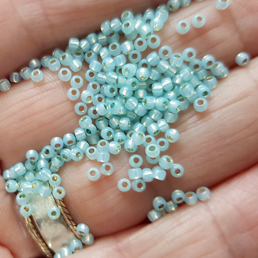 A close up of milky Lt aqua silver-lined Toho seed beads on a human hand
