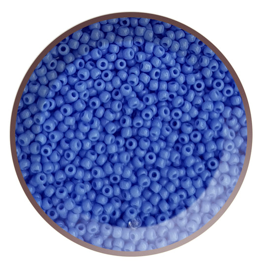 A close-up view of a bowl filled with round, opaque periwinkle blue Toho seed beads.