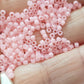 A close-up view of pink frosted round Toho seed beads.11/0 close up on a hand.