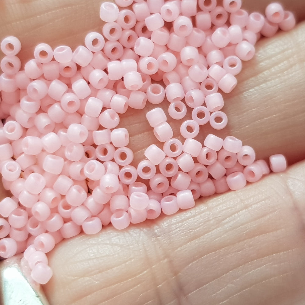 A close-up view of pink frosted round Toho seed beads.11/0 close up on a hand.