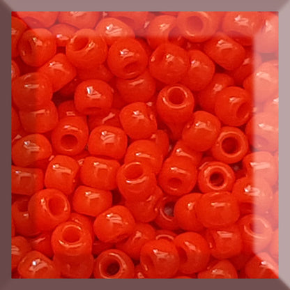 A close-up view of a group of round, opaque sunset orange Toho seed beads.