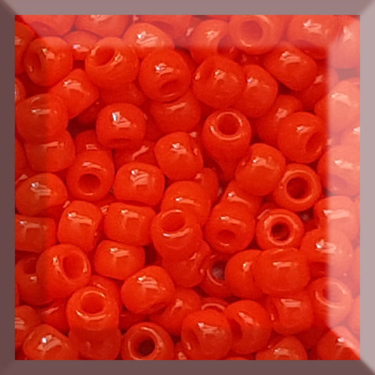 A close-up view of a group of round, opaque sunset orange Toho seed beads.