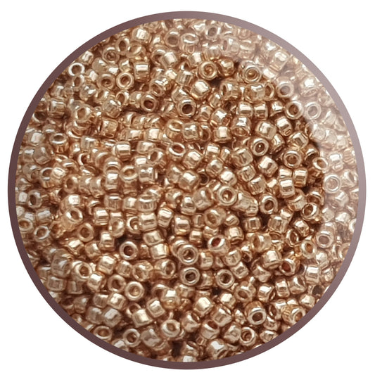 A clear plastic container filled with round rose gold galvanized Toho seed beads 15/0 Permanent Finish.