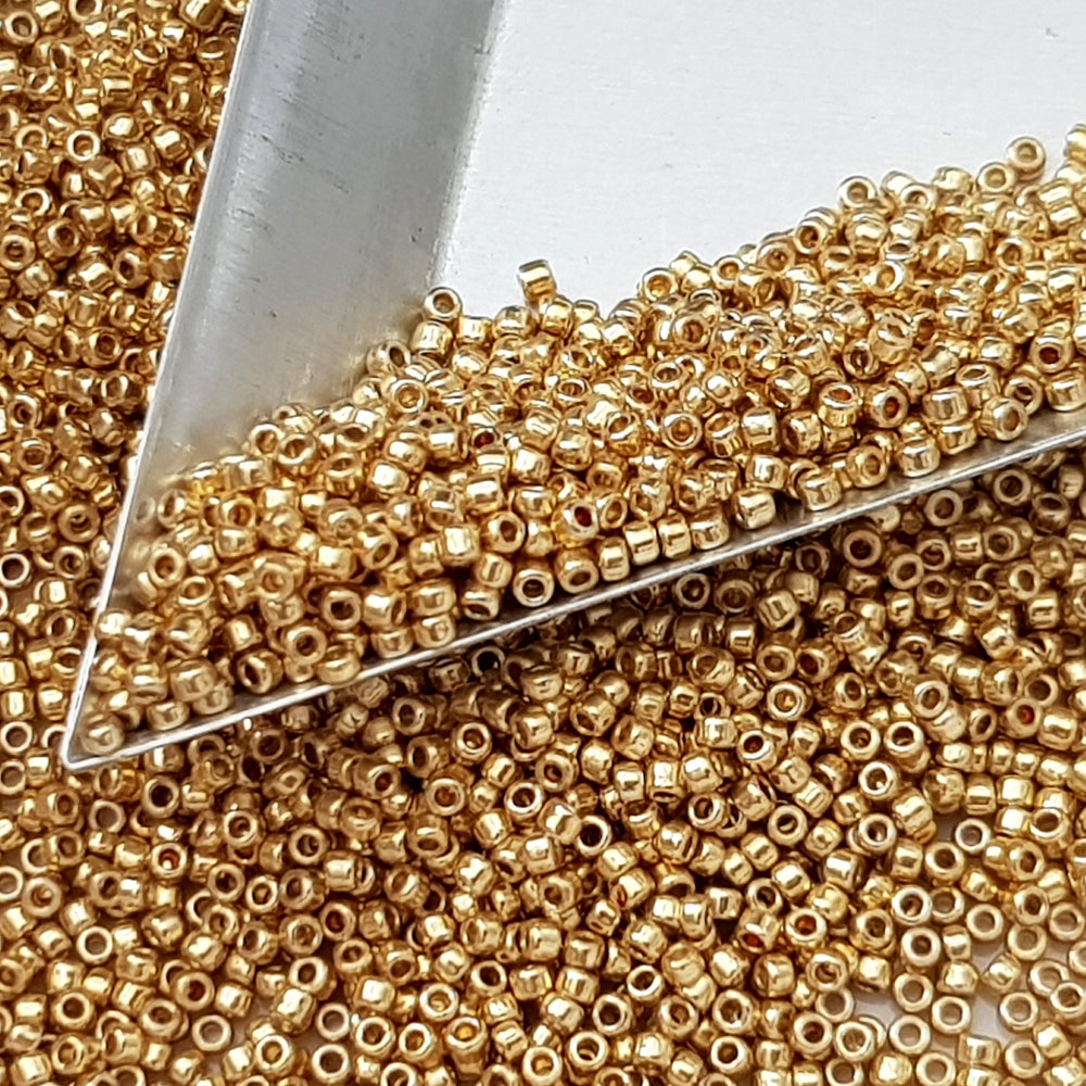 Toho 15/0 starlight gold galvanized permanent finish TR-pf557 with a triangle scoop.