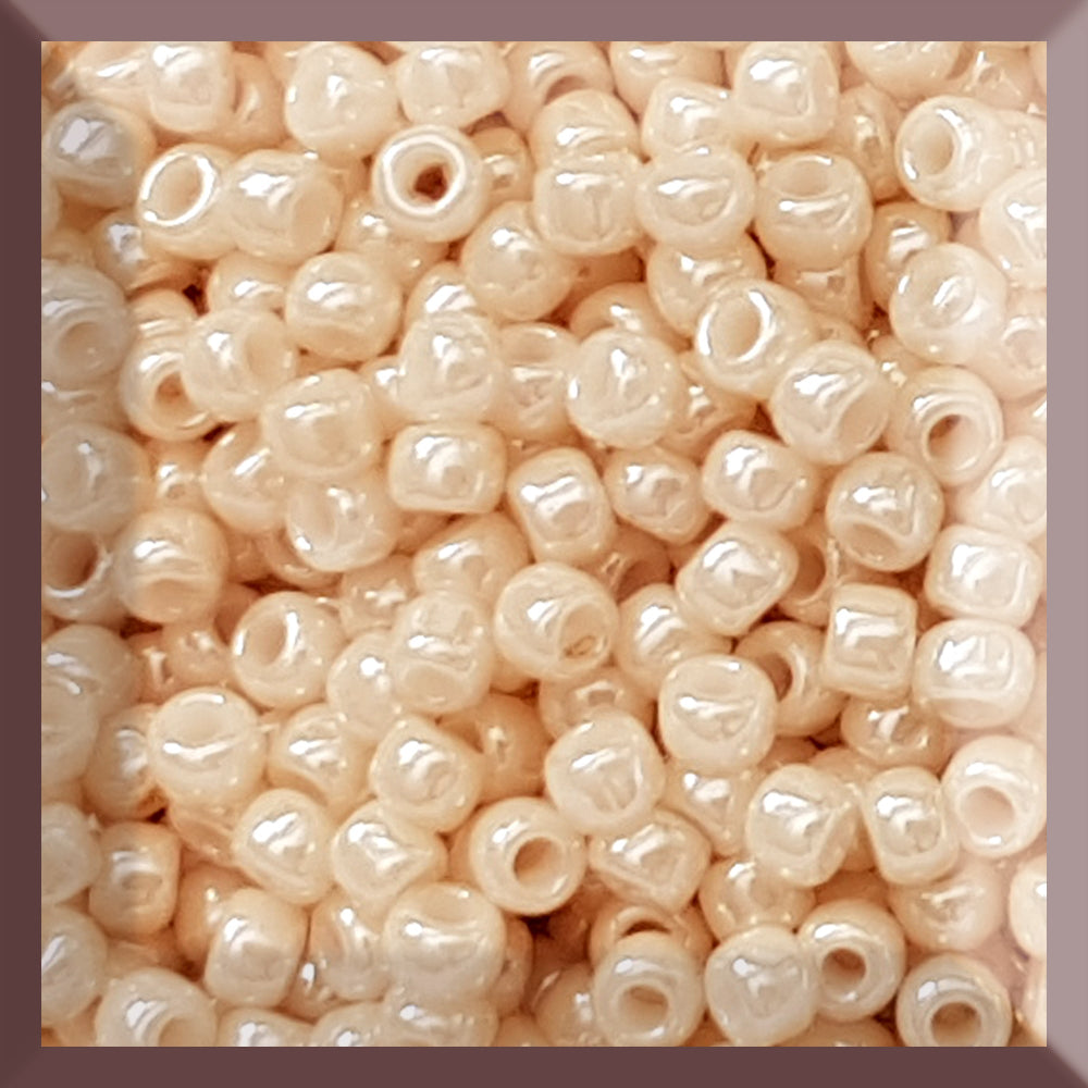 A close-up image of light beige opaque round Toho seed beads. 8/0 TR-123 square window.