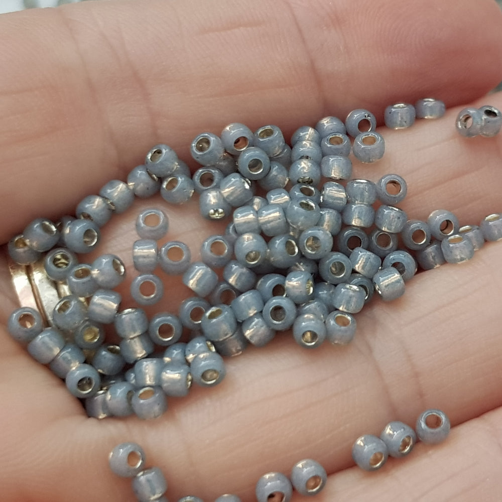 8/0 Toho Seed beads in Milky Grey Silver-Line TR-2115 close up on a hand
